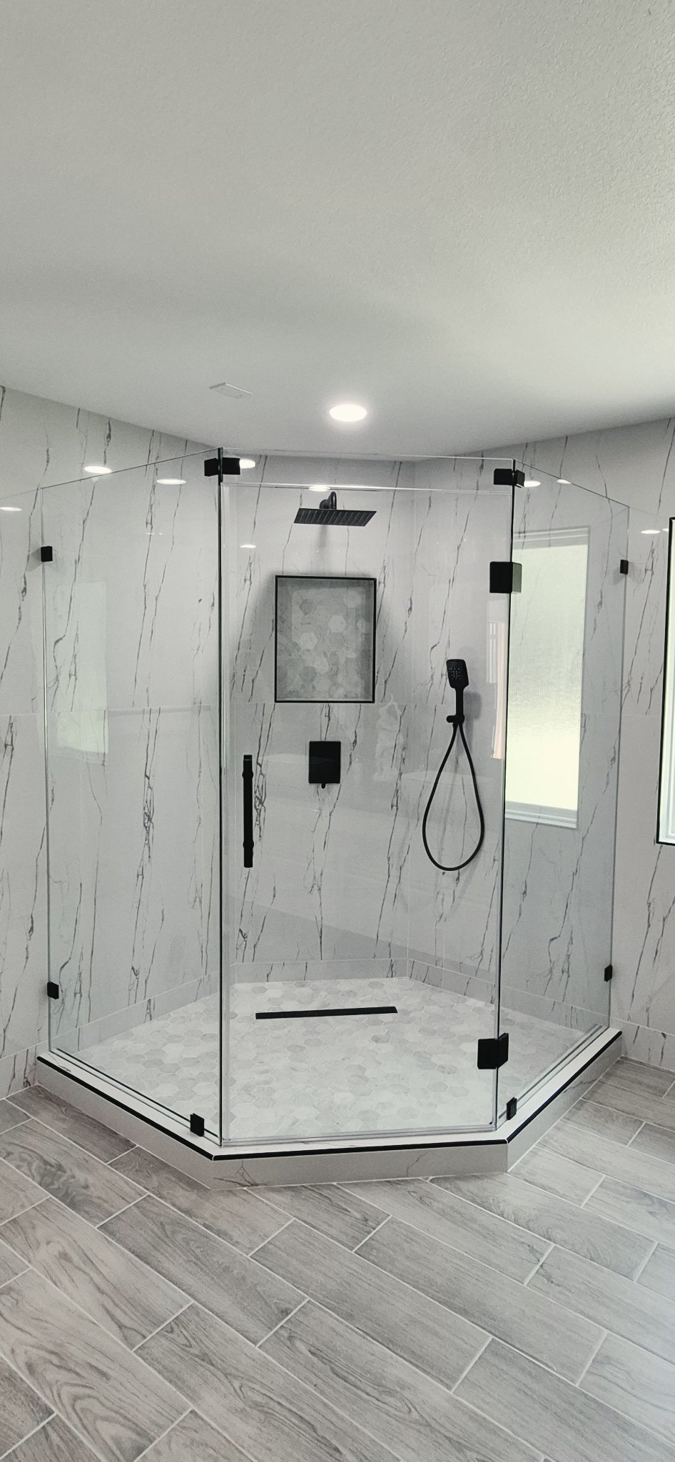 135° angle (neo-angle) bathroom reference photo: glass corner shower with three sides, center door and black hardware, in a bathroom with marble walls