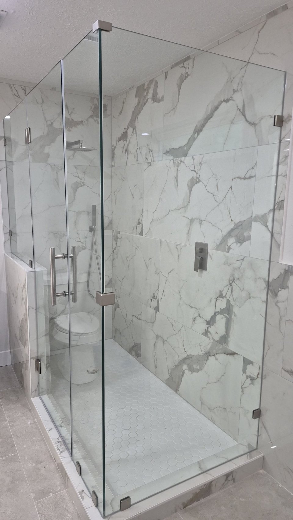 Glas Plus 90° angle over half walls example: clear glass with nickel hardware in a marble bathroom, with one panel mounted on a half wall