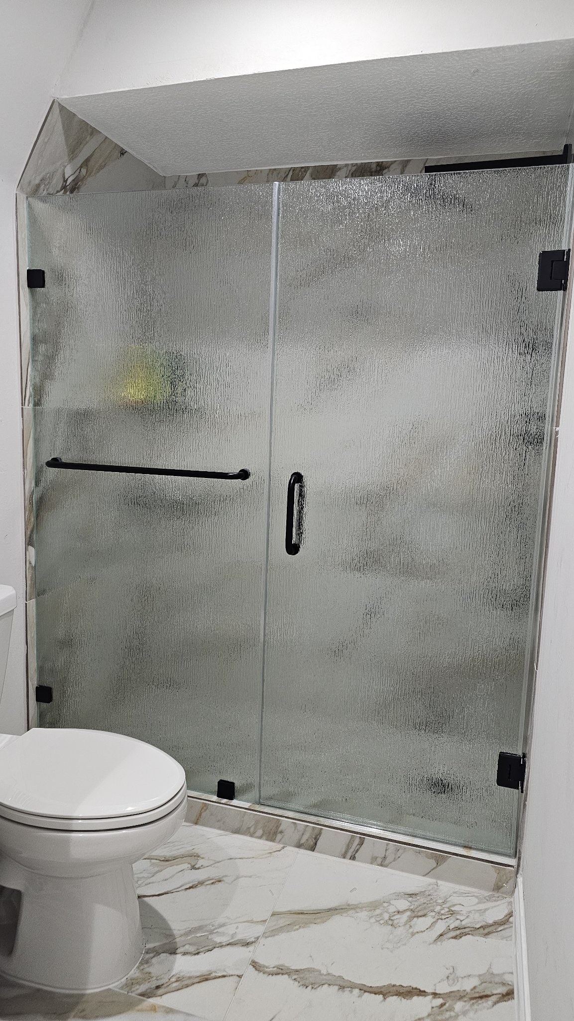 Wall-hinged door with Rain glass (rain texture), fixed panel with towel bar and black hardware in a marble shower