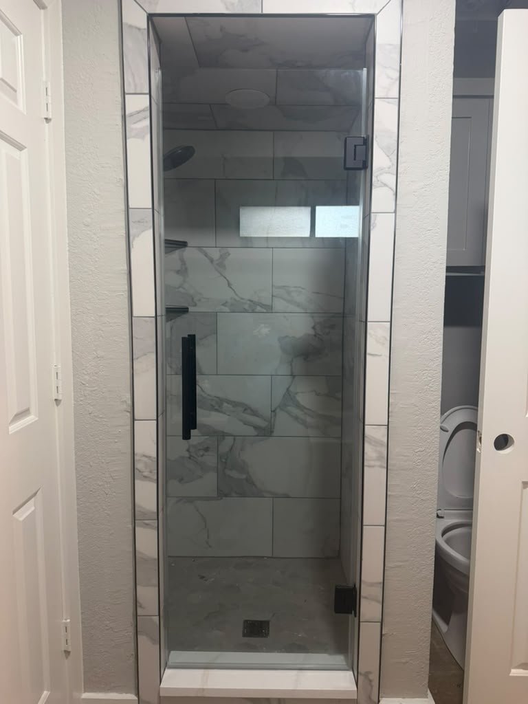 Single door with black hardware installed by Glas Plus in a marble-look tile shower