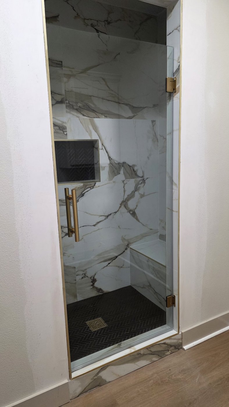 Glas Plus single door reference photo: a single hinged glass door, no panel, with brush gold hardware in a marble shower