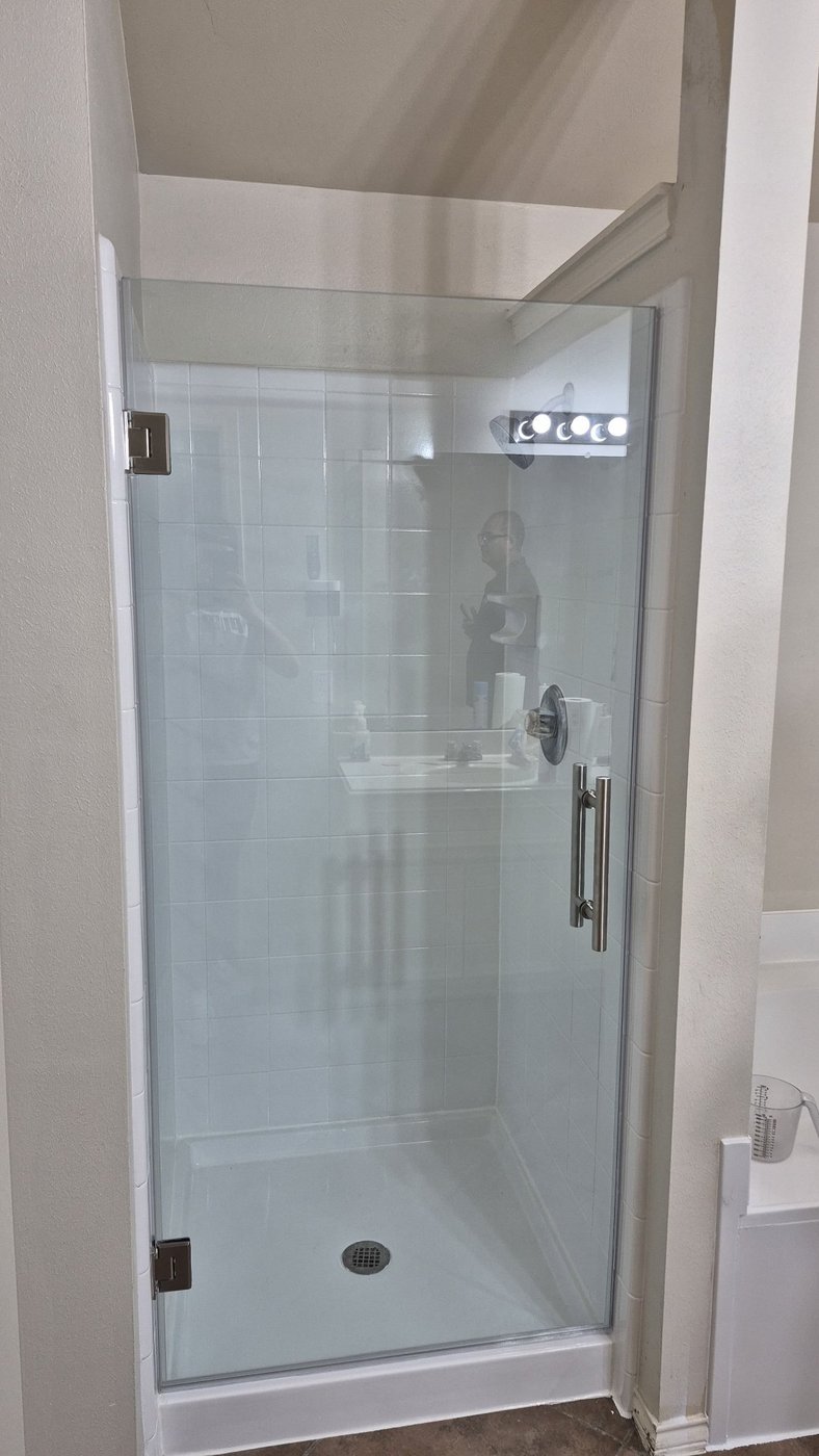 Single door with brush nickel hardware installed by Glas Plus in a white tile shower