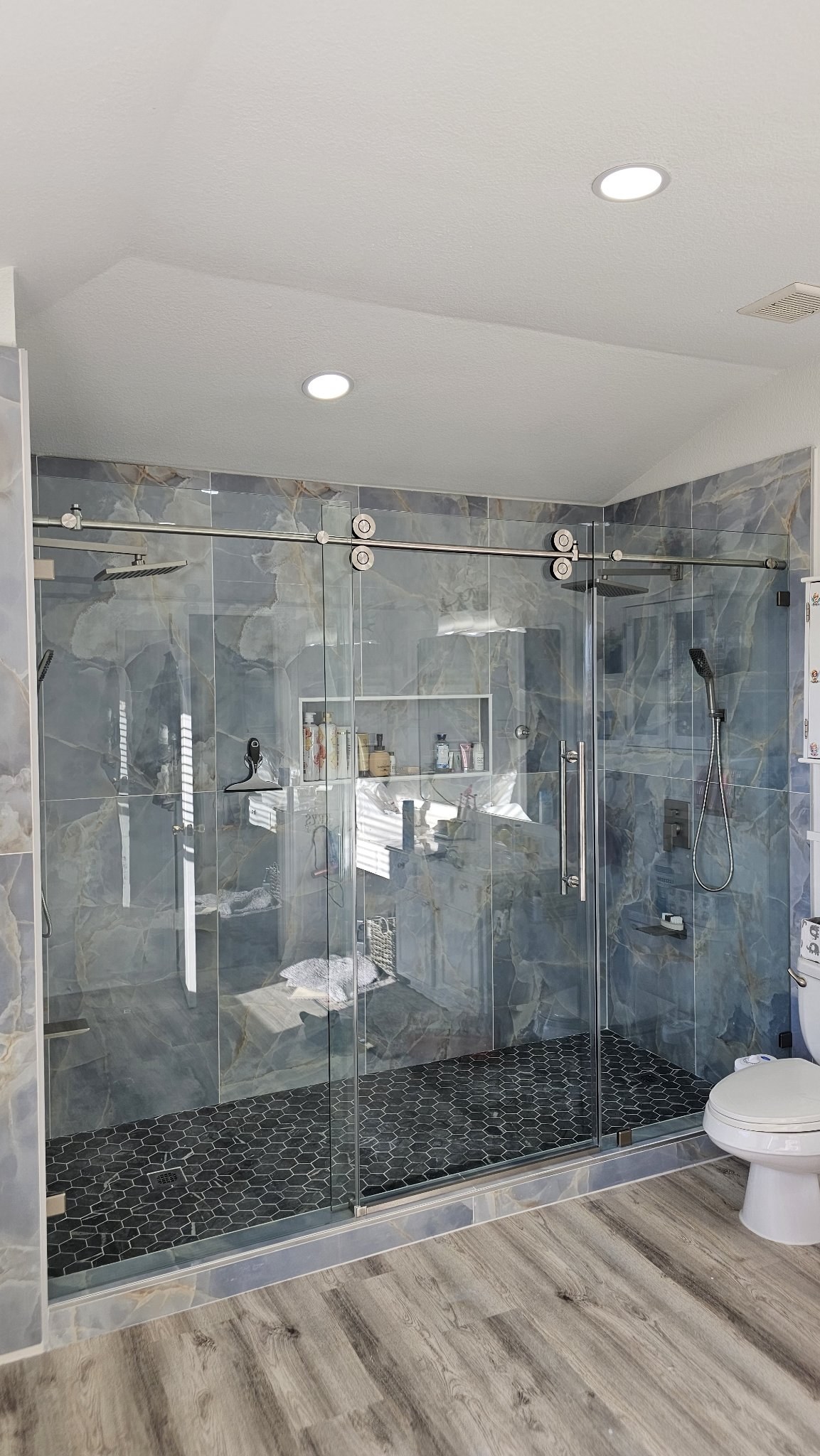 Sliding with center door (fixed panel, door and fixed panel) with a brush nickel track in a blue marble shower with two showers