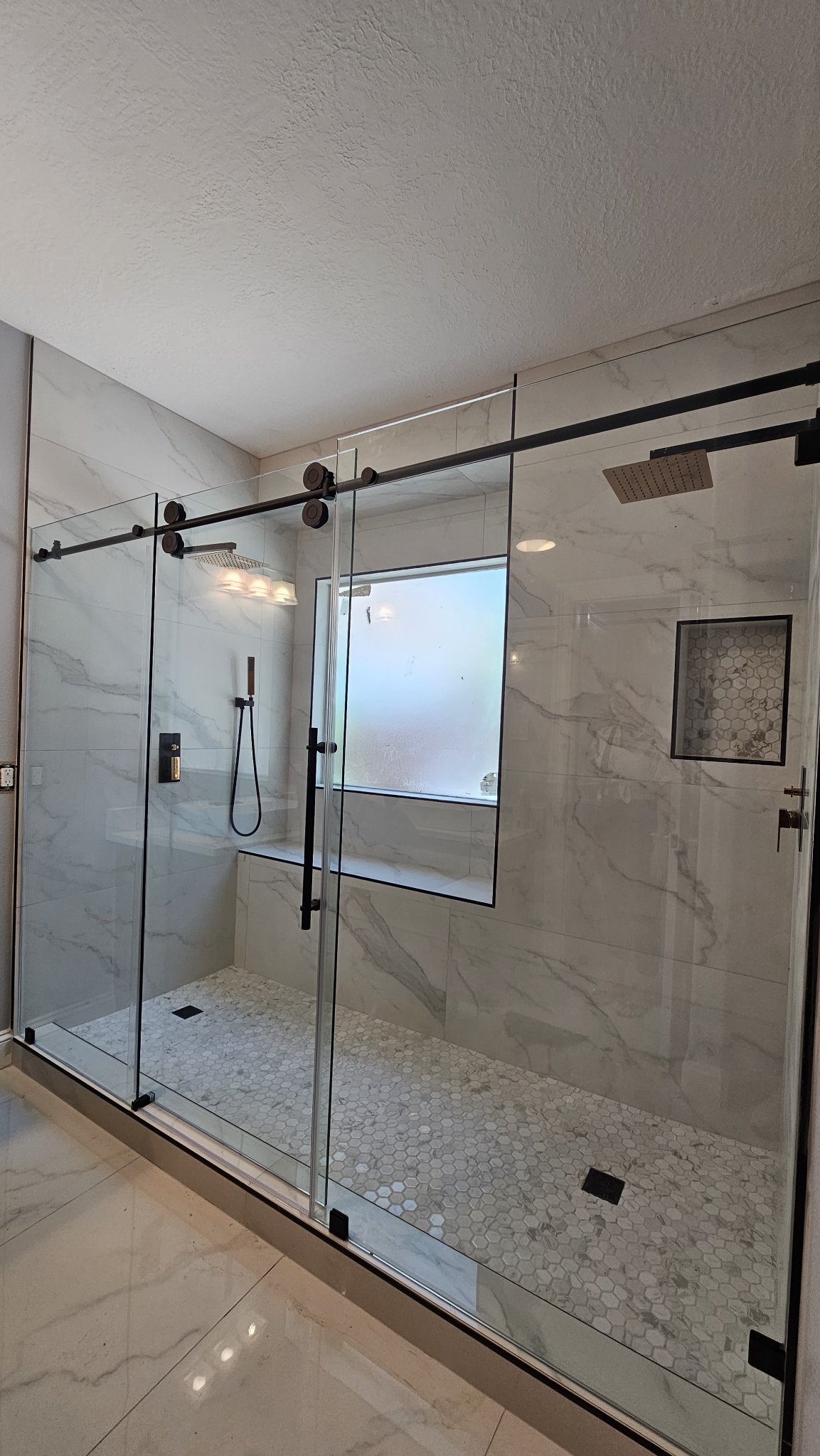 Straight-line sliding with center door reference photo: two fixed side panels and the sliding door in the center on a track, with black hardware, in a large marble bathroom