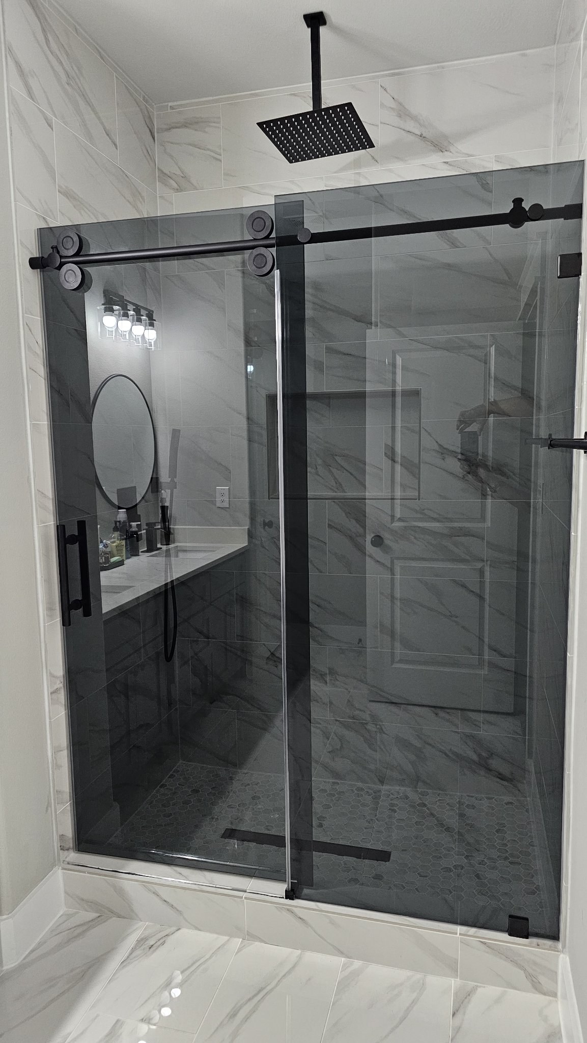 One-door sliding with fixed panel, Grey glass (smoked grey) and black bar in a marble shower with a rain shower head