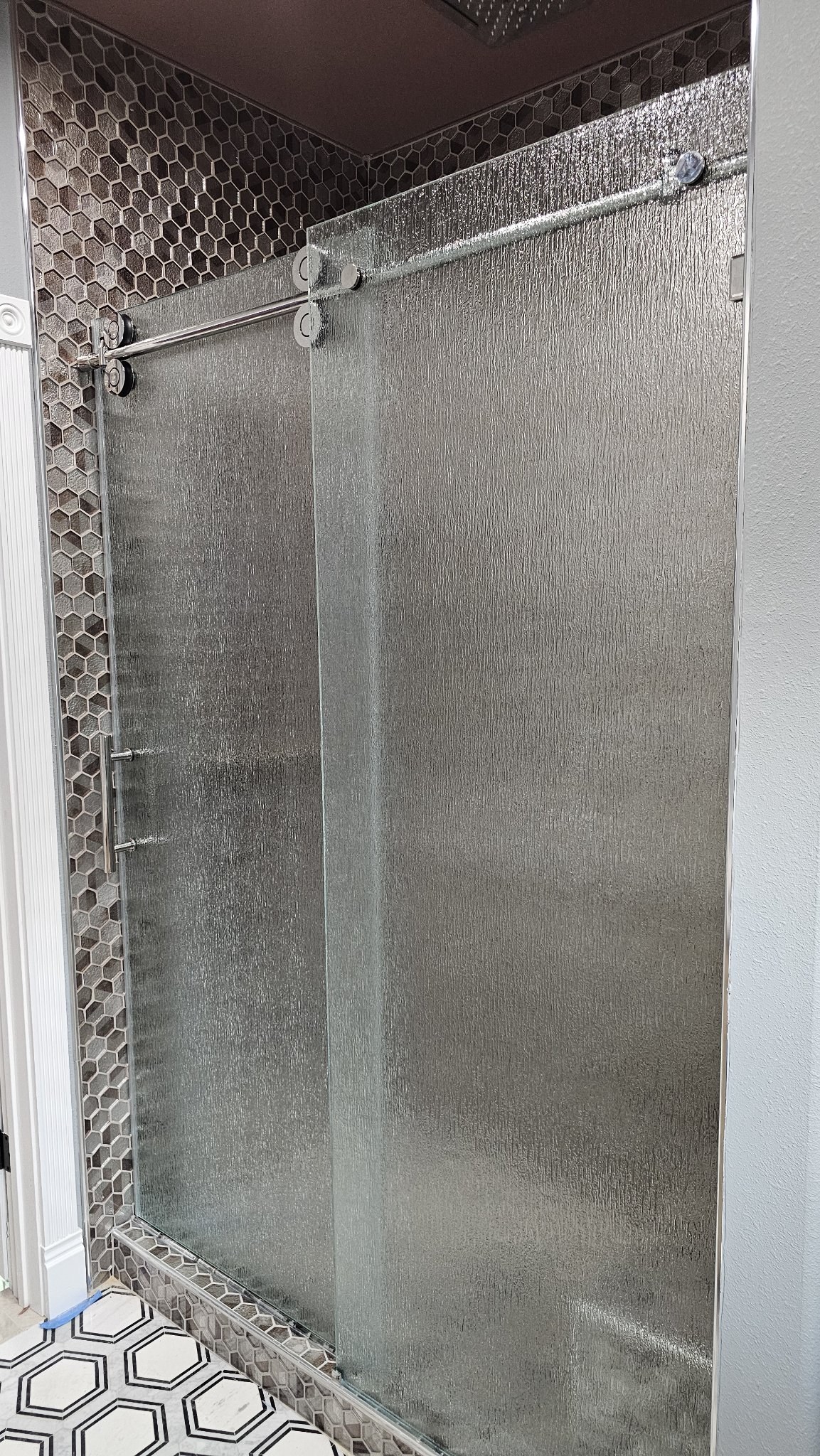 One-door sliding with Rain glass (rain texture), chrome track and fixed panel in a hexagonal tile shower