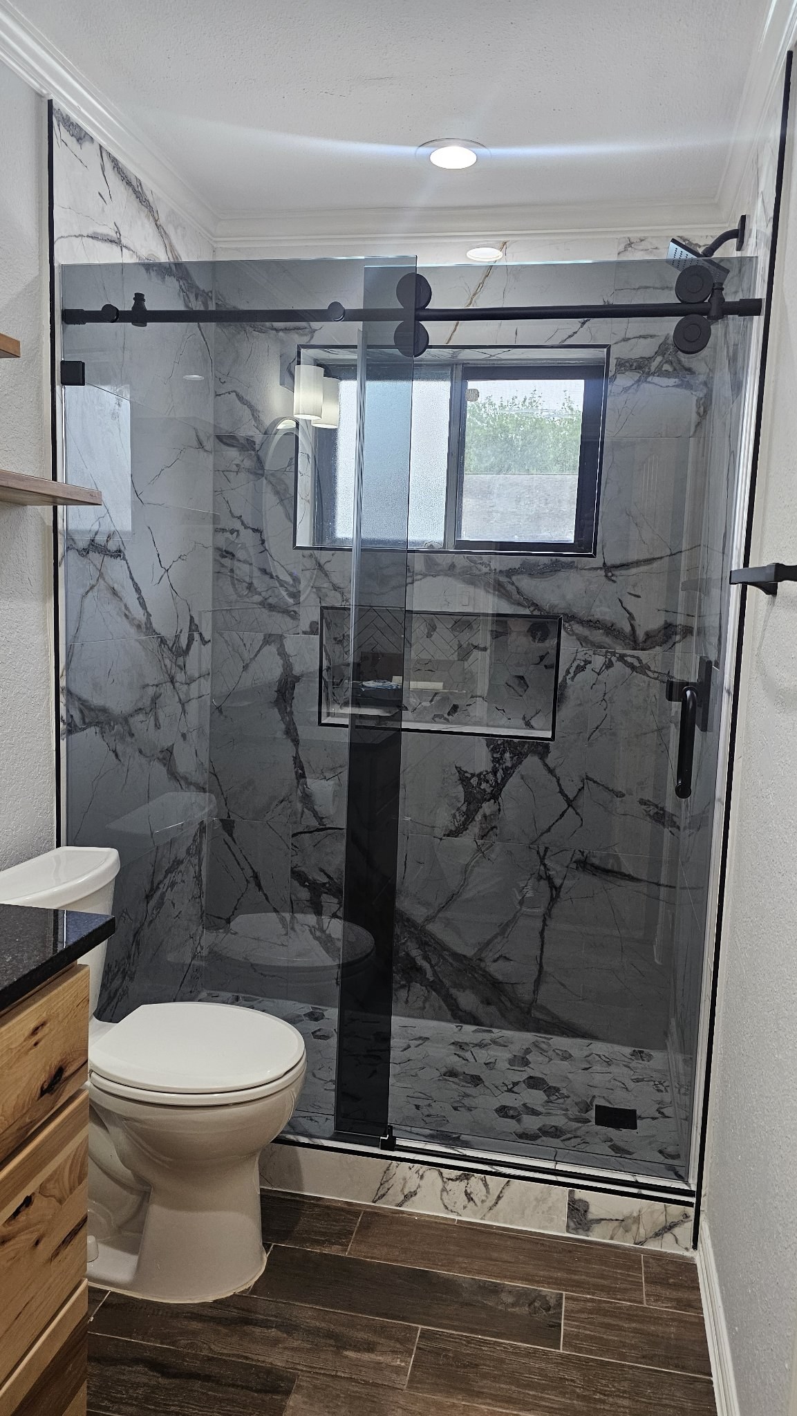 One-door sliding with Grey glass (smoked grey), black bar and fixed panel in a veined marble shower with a niche