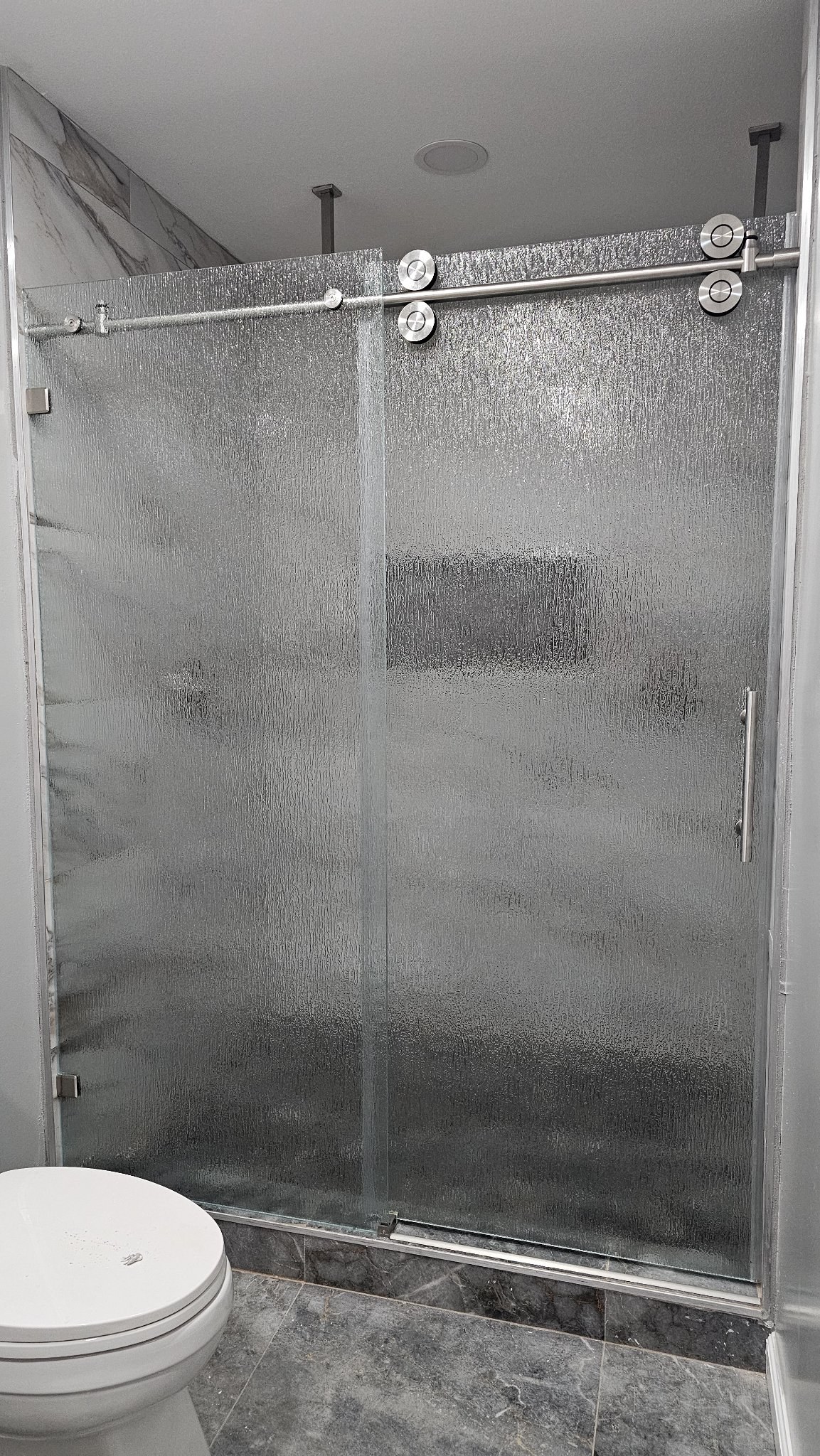 One-door sliding with Rain glass (rain texture), brushed nickel track and fixed panel in a marble tile shower