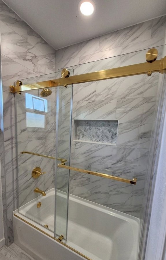 Double-door sliding with gold track over a tub in a beige tile bathroom