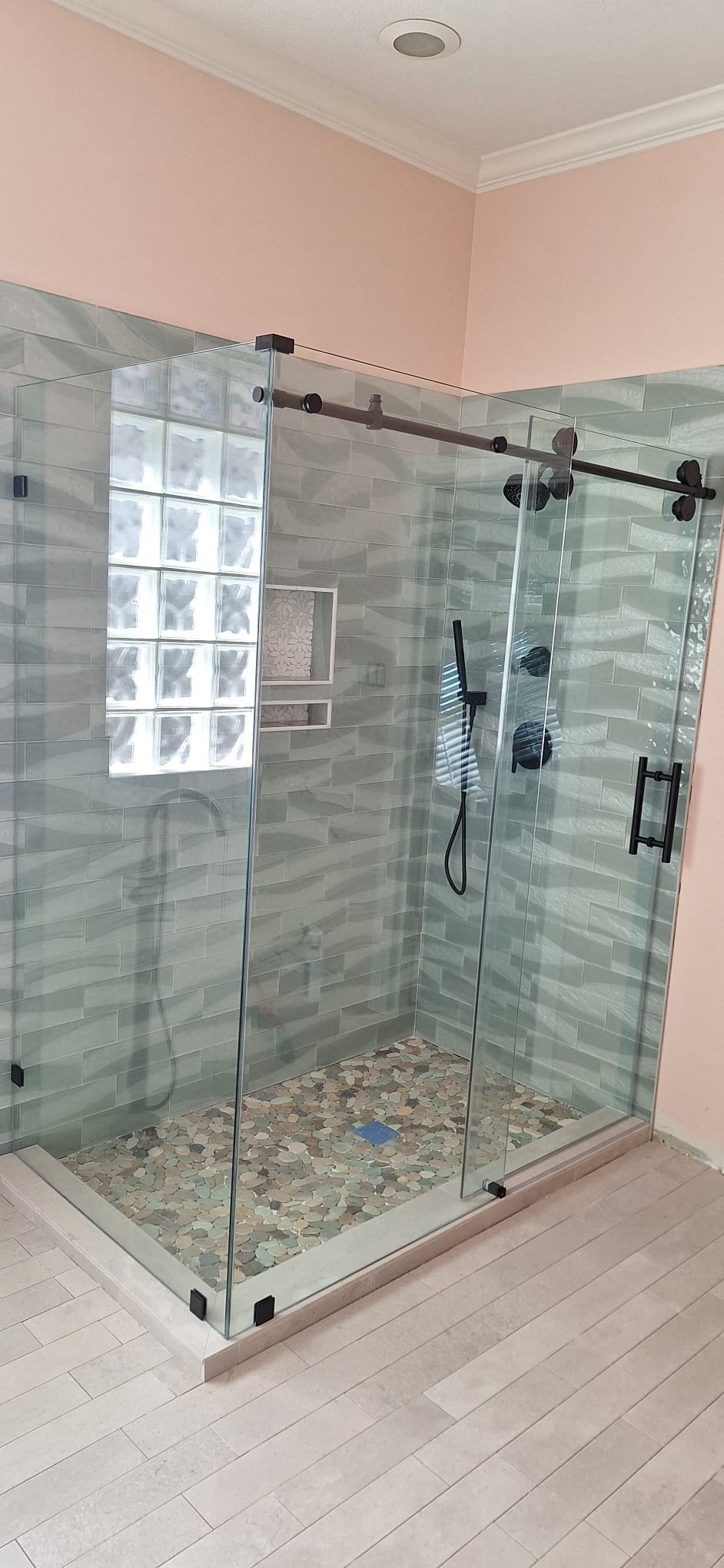 Sliding with return with a black track in a greyish-green tile shower with a glass block window