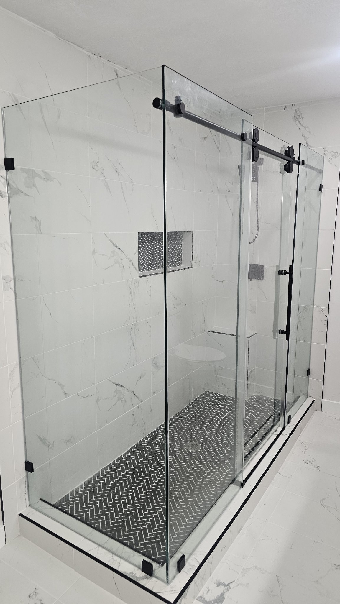 Sliding with return with a black track in a white marble shower with a herringbone floor and niche