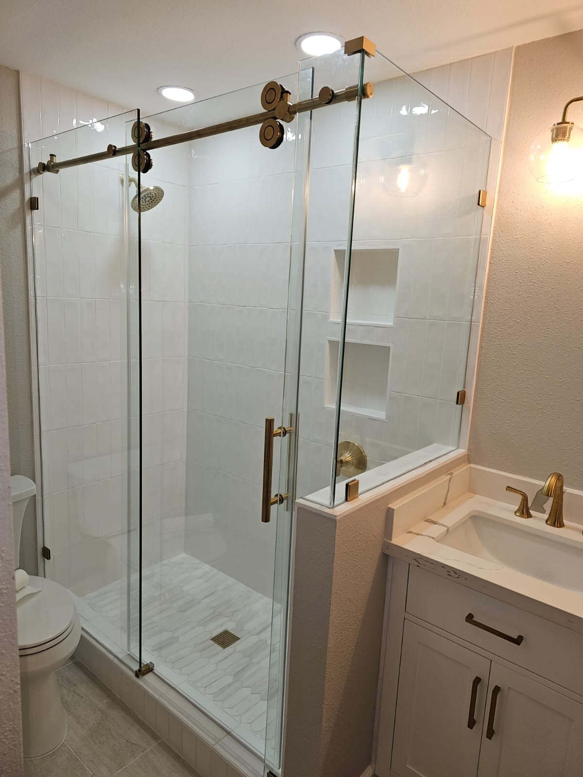 Sliding with return over a half wall with gold track and hardware in a white tile shower with niches