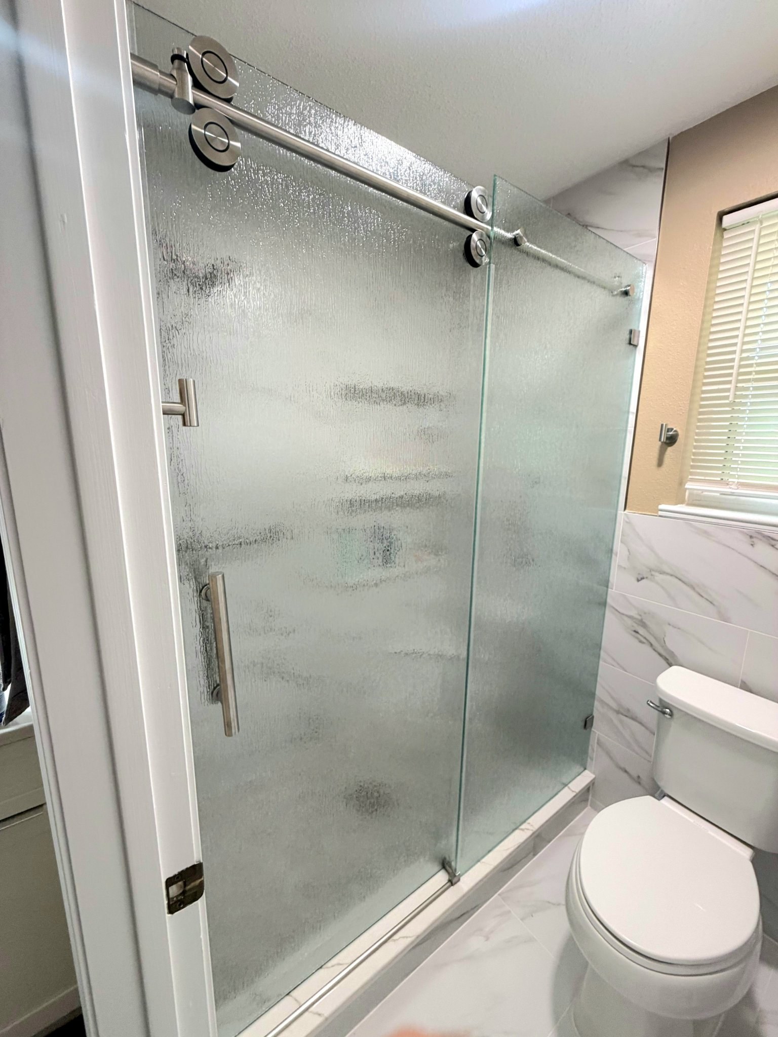 One-door sliding with Rain glass (rain texture), brushed nickel track and fixed panel in a marble tile shower