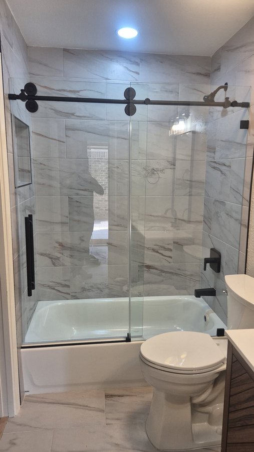 One-door sliding with black track over a tub in a light tile bathroom