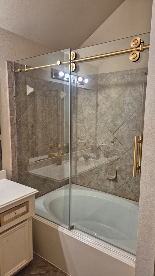 One-door sliding with round gold track over a tub in a beige tile bathroom