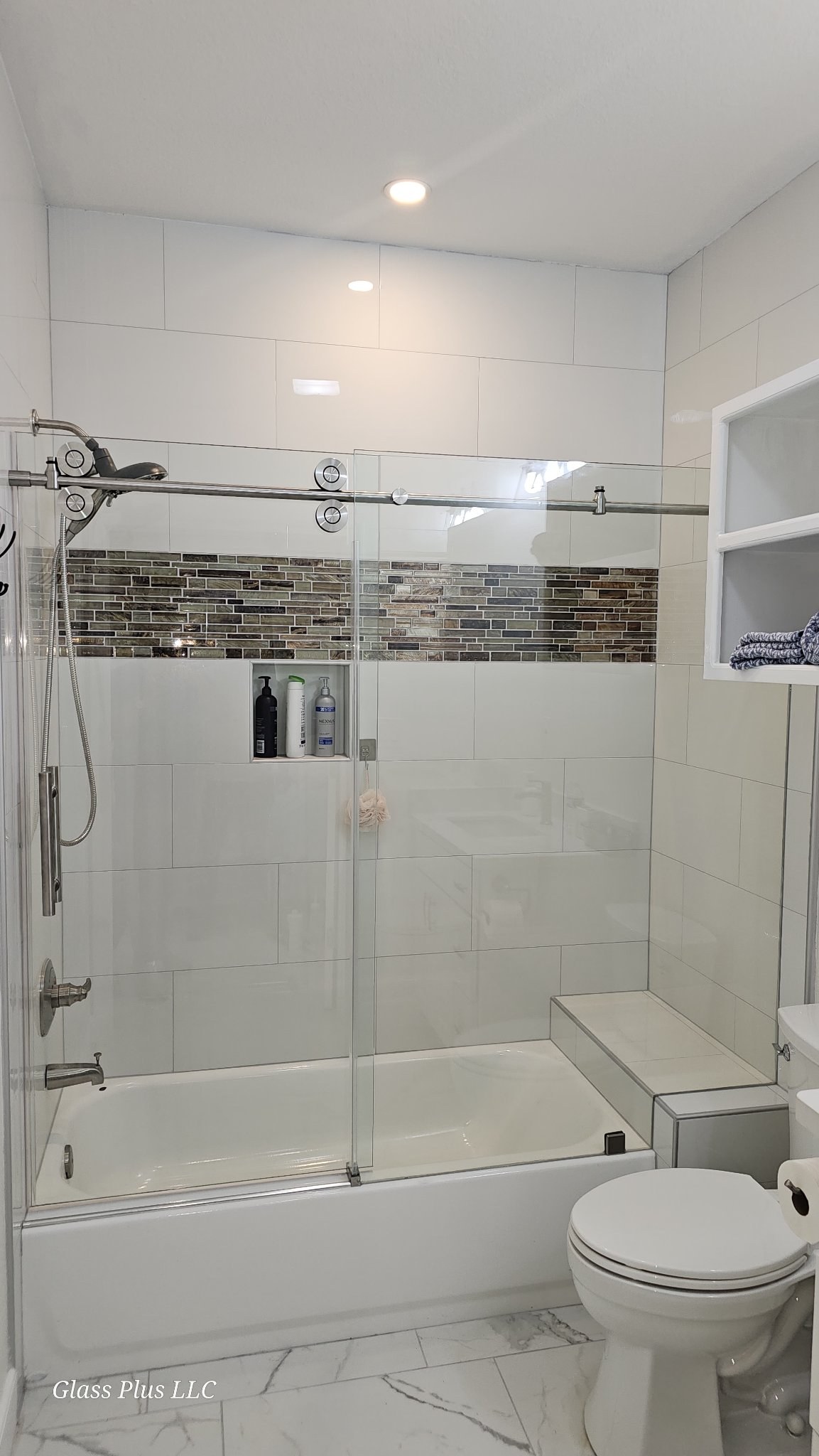 One-door sliding with fixed panel and brush nickel track over a tub in a white tile bathroom with a mosaic band and niche